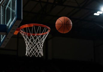 A basketball in mid-air about to enter the hoop in an indoor basketball court with a dark background, captured with sharp focus and professional lighting

