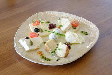 Assortment of cheeses arranged on a plate with olives capers and cherry tomatoes