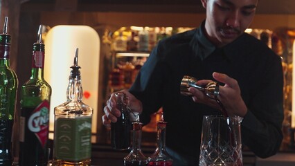 Portrait good looking Asian bartender using jigger measure liquor syrup into mixing glass preparation at luxurious beverage counter bar, neat professional barman costume at nightclub luxury. Vinosity.