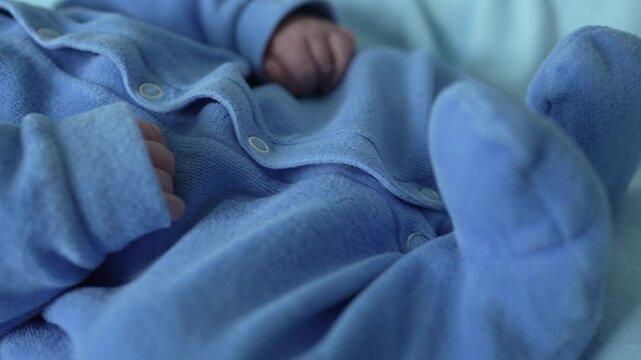 Close-up of a newborn baby&rsquo;s hand and foot, both dressed in a soft blue outfit. The detailed shot highlights the tiny features, showcasing the delicate and precious nature of a newborn