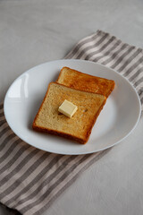 Homemade Toasted Bread Slice with Butter on a Plate, side view.