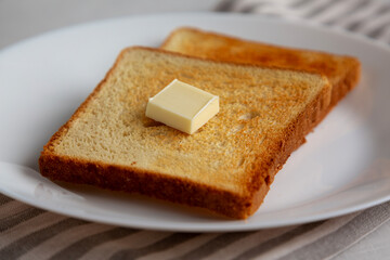 Homemade Toasted Bread Slice with Butter on a Plate, side view.