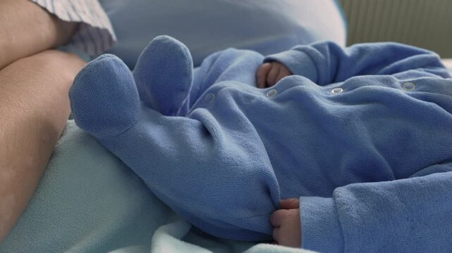 Close-up of a newborn baby resting in a blue onesie,  the sweet and serene moment of sleep. The infant lies on a soft blue blanket, emphasizing the tranquility and purity of early infancy