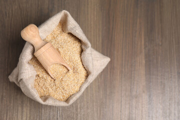 Oat bran and scoop in burlap bag on wooden table, top view. Space for text