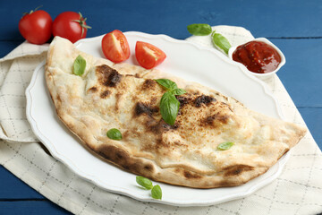 Tasty calzone with basil, tomatoes and sauce on blue wooden table