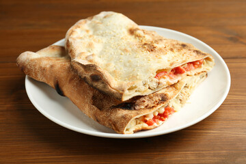 Halves of tasty calzone with meat, cheese and tomato on wooden table, closeup