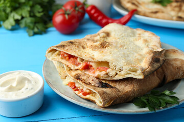 Halves of tasty calzone with meat, cheese, tomato and sauce on light blue table, closeup