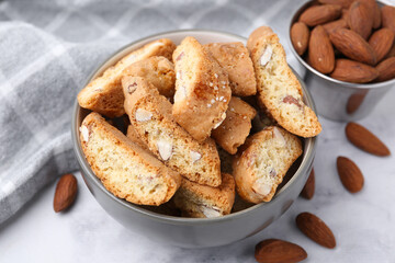 Tasty almond biscuits (Cantuccini) in bowl and nuts on light table, closeup