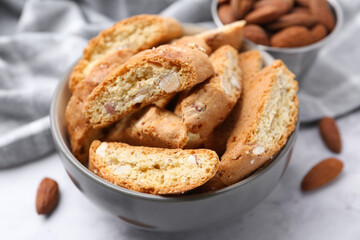 Tasty almond biscuits (Cantuccini) in bowl and nuts on light table, closeup