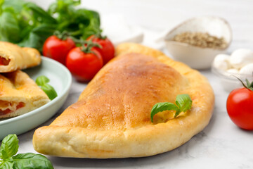 Tasty vegetarian calzone with tomatoes, mozzarella cheese and spices on white marble table, closeup