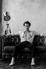 Portrait of a handsome young sexy man in a white shirt, jeans jacket posing in studio with a loft interior. Black and white. Casual clothes, modern style