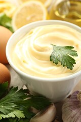 Delicious mayonnaise sauce in bowl and ingredients on table, closeup