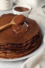 Delicious chocolate crepes with sweet paste on light grey table, closeup