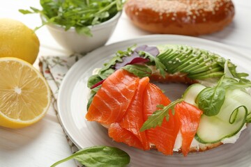 Delicious bagel with salmon, cream cheese, cucumber and avocado on white wooden table, closeup