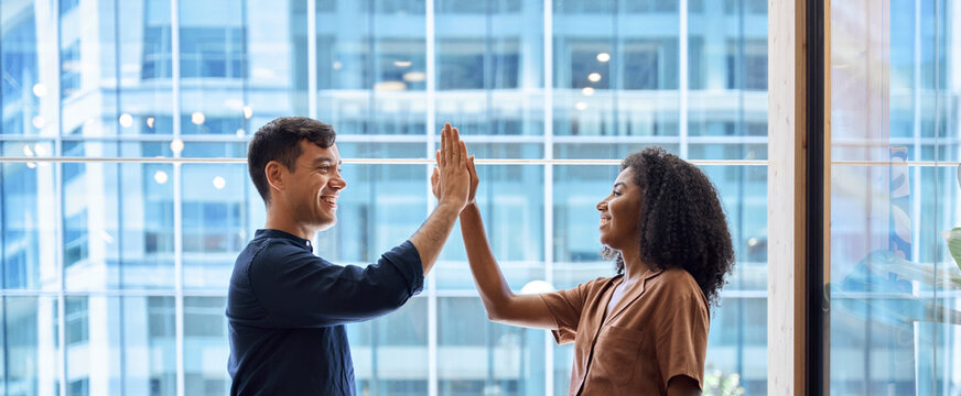 Happy diverse business team man and woman giving high five at work in office. Two partners employees celebrating professional corporate success leadership financial work achievement in office. Banner