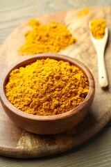 Turmeric powder in bowl on wooden table, closeup