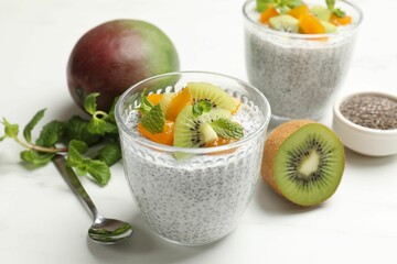 Delicious chia pudding with fruits in glasses, mint and spoon on white table, closeup