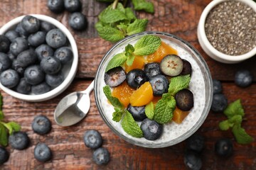 Delicious chia pudding with blueberries, peaches and mint in glass on wooden table, flat lay