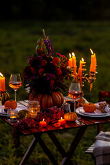 Garden romantic party outside with wine, cheese, fruits. Field or meadow, family event, cozy autumn atmosphere, fall vibes. Wooden furniture, pumpkin with flowers as centrepiece, fresh red dahlia