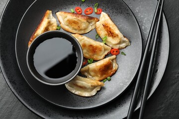 Delicious fried gyoza dumplings with green onions and chili peppers served on black table, top view