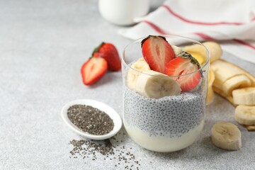 Delicious chia pudding with strawberries and banana in glass on light gray table, closeup. Space for text