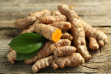 Pile of tumeric rhizomes with leaves on wooden table, closeup