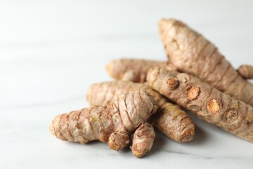 Pile of raw turmeric roots on white marble table, closeup. Space for text