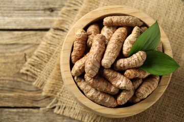 Tumeric rhizomes with leaves in bowl on wooden table, top view