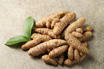 Pile of tumeric rhizomes with leaves on grey table, closeup
