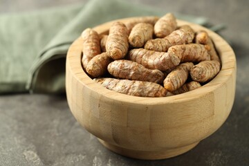 Tumeric rhizomes in bowl on grey table, closeup