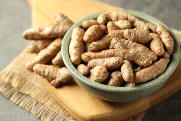 Tumeric rhizomes in bowl on grey table, closeup