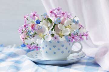 Beautiful bouquet with spring blooming apple flowers, forget-me-nots, subulate phlox in a cup on the table. Romantic postcard.