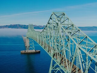 Fototapeta premium A long, green steel Astoria-Megler Bridge spans a body of water, with fog in the distance. The intricate design of the bridge's structure is highlighted. Astoria, Oregon, USA