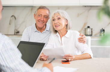 Elderly couple listens attentively to insurance manager while at home. Health insurance concept