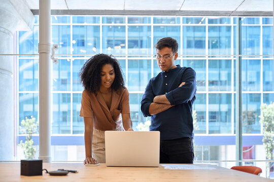 Two busy business people man and woman working on computer discussing online project at work. Diverse professional workers team talking on financial technology or marketing data using laptop in office