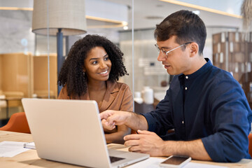 Two young busy diverse coworkers business people using laptop at office meeting. Smiling team...