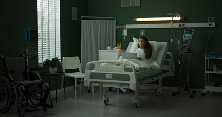 Patient in a hospital room uses a laptop while resting in bed.