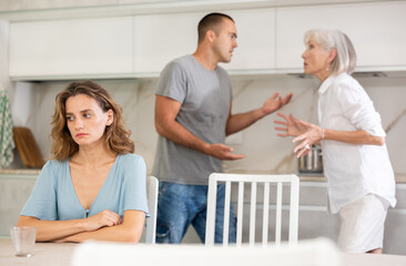 Obraz premium Elderly woman gets angry during quarrel with man and woman couple in kitchen