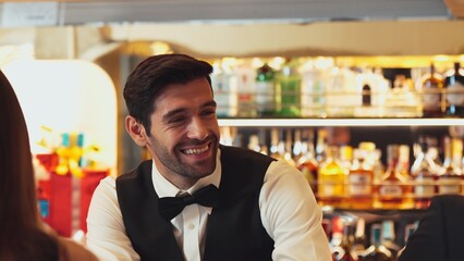 Good looking bartender warm smiling friendly conversation with couple customer at beverage bar counter while serving welcome drink with charm professionalism recommending special menu list. Vinosity.