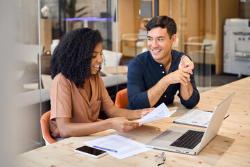 Two young diverse business people using laptop and talking at office meeting. Busy happy team...