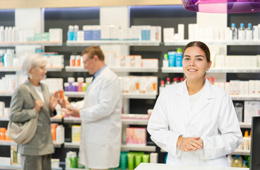 Obraz premium Positive young girl pharmacist posing in chemist's shop with large assortment of goods