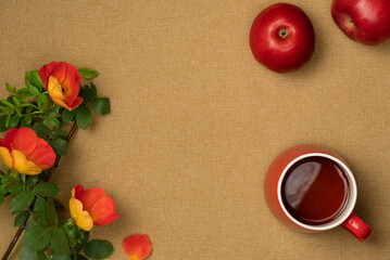 Rosehip flowers with cup of tea and apples on fabric background. Flat lay, top view. Copy space