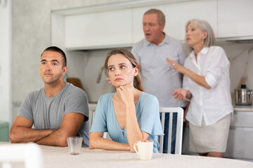 Girl and guy are sitting in kitchen and do not listen to their father and mother