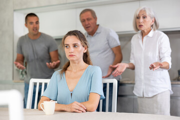 Young girl sits at table in kitchen in thought without hearing her family