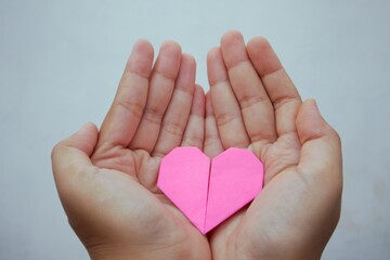 Woman's hand holding pink love shape origami paper