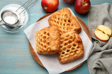 Delicious puff pastries, apples and powdered sugar on light blue wooden table, top view