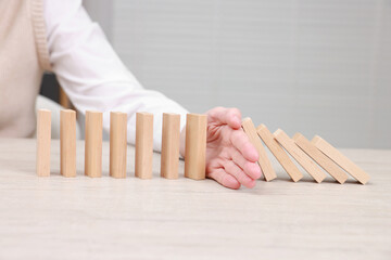 Woman stopping wooden blocks from falling at table, closeup. Domino effect