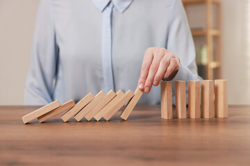 Woman stopping wooden blocks from falling at table, closeup. Domino effect