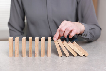 Woman stopping wooden blocks from falling at table, closeup. Domino effect