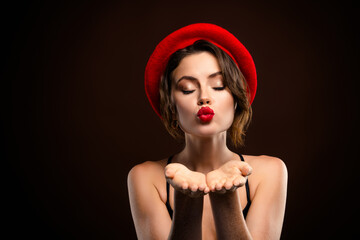 Charming woman wearing a red beret blows a kiss against a dark backdrop